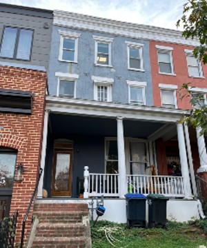 Light blue row house with white trim and red brick stairs, showing some wear on the front facade.